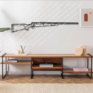 以下が含まれることがあります： 白い壁に黒い金属製のライフルのシルエットの壁飾り。その下に黒い金属製の脚が付いた木製の棚があり、本や装飾品が置かれている。