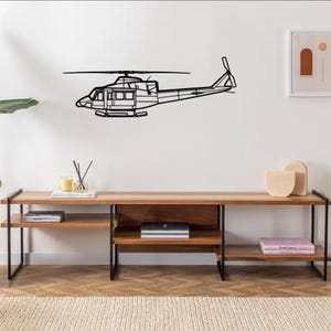 May include: A black metal helicopter wall art piece. The helicopter is depicted in a side profile, with detailed outlines of the body, rotor, and tail. It is mounted on a white wall above a wooden console.