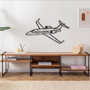 May include: A black metal wall art piece depicting a private jet. The artwork is mounted on a white wall above a wooden console table. The jet has detailed wings, tail, and engine components, creating a modern, minimalist aesthetic.