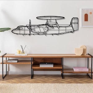 May include: Black metal wall art depicting a plane with a propeller and a radar dish. The art is mounted on a white wall above a wooden shelf with books and decorative objects.