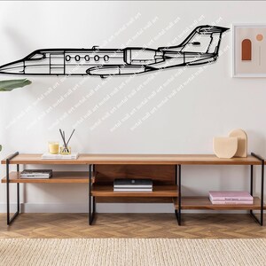 May include: A black metal wall art piece depicting a private jet. The artwork is mounted on a white wall above a wooden media console with black metal legs. A framed abstract art print and decorative items are also present.
