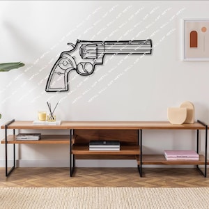 Könnte beinhalten: Eine schwarze Wanddekoration aus Metall in Form einer Revolverpistole. Die Dekoration ist an einer weißen Wand über einem Holzregal mit schwarzen Metallbeinen angebracht. Das Regal enthält Bücher und Dekorationsgegenstände.