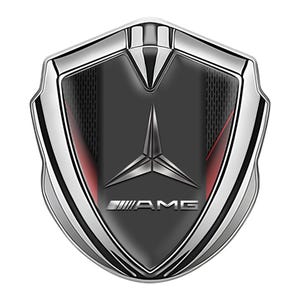 Puede incluir: Un emblema AMG cromado y negro, con forma de escudo. El emblema presenta una estrella de tres puntas y el logotipo AMG. Se ven detalles rojos en los lados del emblema.