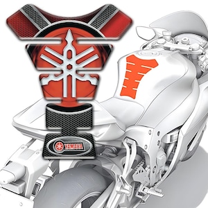 Puede incluir: Una motocicleta blanca con un protector de tanque Yamaha rojo y negro. El protector tiene el logotipo de Yamaha y un patrón de panal. La motocicleta tiene detalles en naranja.