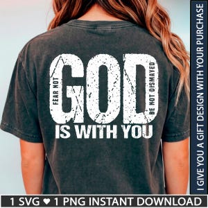 Puede incluir: Una camiseta de manga corta gris carbón con letras blancas desgastadas en la espalda. El texto dice GOD IS WITH YOU, con las frases FEAR NOT y BE NOT DISMAYED integradas en el diseño. La camiseta tiene un acabado de lavado vintage.