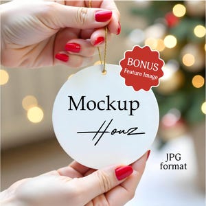 Könnte beinhalten: Ein weißer, runder Ornament mit dem Text "Mockup Houz" in schwarzer Schrift. Das Ornament wird von Händen mit rotem Nagellack gehalten. Ein roter "BONUS Feature Image" Aufkleber ist sichtbar. Ein goldener Faden ist befestigt.