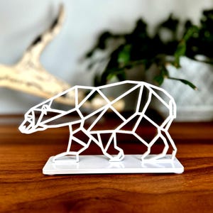May include: A white geometric polar bear sculpture. The bear is made of interconnected lines, creating a modern, minimalist design. It stands on a small, rectangular base, ideal for a desk or shelf.