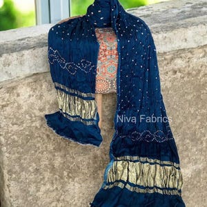 Op de afbeelding: Een marineblauwe stoffen set, inclusief een sjaal en een top met patroon, gedrapeerd op een mannequin. De sjaal heeft gouden accenten en witte stippenpatronen. De top heeft een kleurrijk, ingewikkeld ontwerp. De tekst "Niva Fabrics" is zichtbaar.