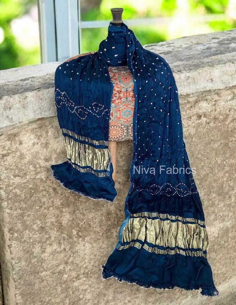 Op de afbeelding: Een marineblauwe stoffen set, inclusief een sjaal en een top met patroon, gedrapeerd op een mannequin. De sjaal heeft gouden accenten en witte stippenpatronen. De top heeft een kleurrijk, ingewikkeld ontwerp. De tekst "Niva Fabrics" is zichtbaar.