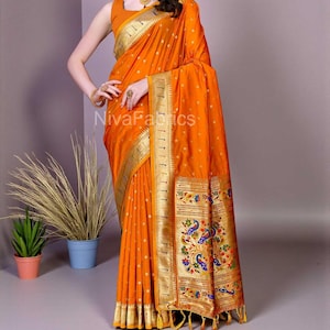 Puede incluir: Un sari naranja con ribete dorado y un borde decorativo con diseños de pavo real. El sari tiene pequeños puntos blancos y el texto "NivaFabrics" es visible.