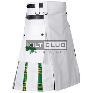 Op de afbeelding: Witte kilt met zwarte leren riemen en gespen. De kilt heeft een groen en geel geruit patroon aan de zoom en een zak met een groene klaver. De tekst "KILT CLUB" en "ETS KILT" is zichtbaar.