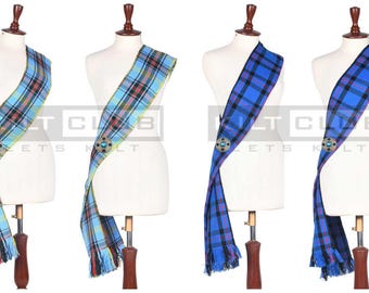 Op de afbeelding: Vier tartan sjerpen in lichtblauw en blauw, tentoongesteld op mannequins. Elke sjerp heeft een ruitpatroon met franjes aan de onderkant en een decoratieve broche. De sjerpen zijn over de mannequins gedrapeerd, waarbij het ontwerp en de textuur worden getoond.