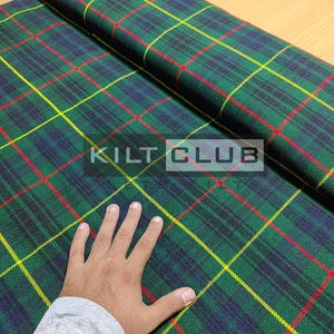 May include: Green, blue, red, and yellow plaid fabric with the text "KILT CLUB". The fabric is folded over, showing the pattern in detail. The plaid design is a classic pattern, often used for kilts and other traditional garments.