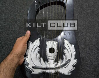 Może przedstawiać: Czarna lira ze srebrnymi akcentami i strunami. Instrument posiada dekoracyjny wzór i napis "KILT CLUB" w białym prostokącie. Lira jest trzymana przez dłoń na ciemnoszarym tle.