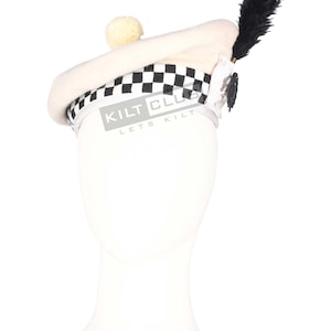 Puede incluir: Un gorro escocés color crema con una banda a cuadros blancos y negros. El sombrero presenta un pequeño pompón esponjoso y una pluma negra. El texto "KILT CLUB LETS KILT" está impreso en la banda.