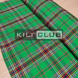 May include: Green plaid fabric with red, yellow, and black accents. The fabric is folded over, revealing the pattern. The text "KILT CLUB" is visible in a white box. The fabric is likely used for kilts or other Scottish-themed apparel.