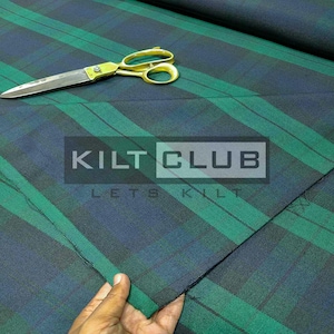 May include: Green and navy blue plaid fabric with gold scissors. The fabric has a bold stripe pattern and the text "KILT CLUB" is visible. The fabric is likely for kilts or other Scottish-themed projects.