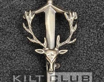 May include: Silver kilt pin with a sword design, deer head, and antlers. The pin has a twisted handle. The text "KILT CLUB" is visible.