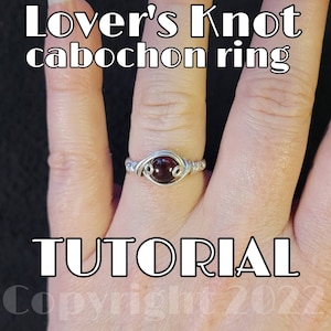 Puede incluir: Un anillo de alambre plateado envuelto con una piedra cabujón roja. El anillo está en una mano y el texto "Lover's Knot cabochon ring TUTORIAL" está debajo de la mano.