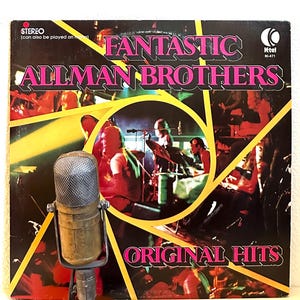 May include: Vintage vinyl record album cover for "Fantastic Allman Brothers: Original Hits." The album cover features the band's name in pink and the album title in pink and white. A vintage microphone is in the foreground.