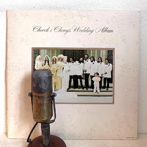 May include: Vintage vinyl record album cover for "Cheech & Chong's Wedding Album." The cover features a photo of a wedding party and the album title in script. An antique microphone is in the foreground.