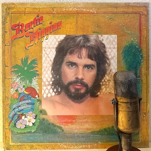 May include: Vintage Bertie Higgins album cover featuring a portrait of the artist. The album art has a tropical theme with a parrot, palm trees, and the text "Just Another Day in Paradise."