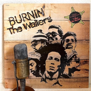 May include: Vintage album cover for "Burnin'" by The Wailers, featuring a group portrait in black and white. The album art is set against a wooden background. A vintage microphone is in the foreground.