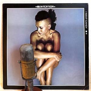 May include: Album cover for "I Want Candy" by Bow Wow Wow. The cover features a woman with gold body paint, seated with her knees drawn up. An antique microphone is in the foreground. The album title and band name are visible.