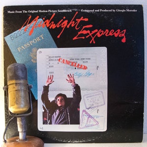 May include: A vintage vinyl record album cover for the soundtrack to the movie "Midnight Express". The cover features a passport with a red stamp that says "CANCELLED" and a photo of a man with his arms raised in the air. The album cover is black with red and white text.