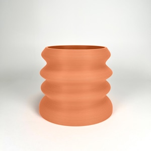 May include: A terracotta-colored ceramic planter with a wavy, ribbed design. The planter is cylindrical and has a wide opening.