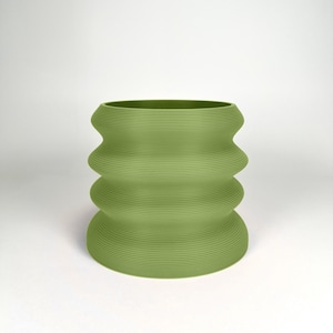 May include: A green ceramic planter with a wavy, ribbed design. The planter is cylindrical and has a wide opening.