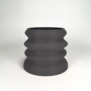 May include: A dark gray ceramic planter with a wavy, rippled design. The planter has a wide, round opening and a slightly narrower base.
