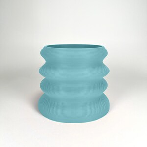 May include: A light blue ceramic planter with a wavy, rippled design. The planter is made of a smooth, textured material.