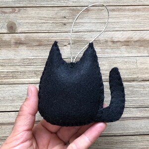 Op de afbeelding: Zwarte vilt katten ornament met een lus om op te hangen. De kat zit met zijn staart om zijn lichaam gekruld.