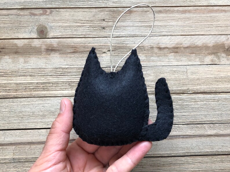 Op de afbeelding: Zwarte vilt katten ornament met een lus om op te hangen. De kat zit met zijn staart om zijn lichaam gekruld.