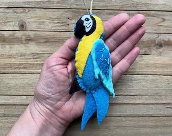 Può includere: Un ornamento di pappagallo in feltro blu e giallo con occhi neri. Il pappagallo è appeso a una corda.