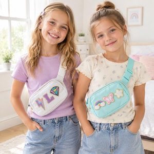 May include: A white fanny pack with a lightning bolt, letter L, and diamond patch, and a light blue fanny pack with a rainbow, butterfly, and star patch. Both bags feature adjustable straps with side-release buckles and zippered main compartments.
