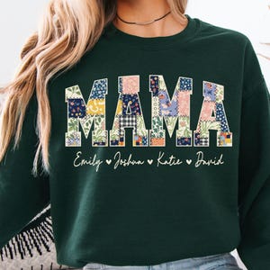 May include: Dark green sweatshirt featuring the word "MAMA" in a patchwork design. The letters are filled with floral and patterned fabrics. Below "MAMA" are the names "Emily", "Joshua", "Katie", and "David".