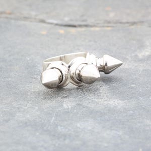 May include: A silver ring with three pointed spikes. The ring is designed with two spikes on the top and one on the side.