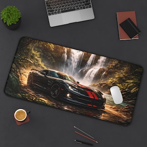May include: Black desk mat featuring a black sports car with red racing stripes, set against a backdrop of a waterfall and lush greenery. A white mouse, laptop, and coffee cup are also visible.