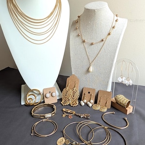 May include: A collection of gold-toned jewelry including a multi-strand chain necklace, a pendant necklace with beads, hoop earrings, drop earrings, stud earrings, a textured ring, a link bracelet, a cuff bracelet, and several thin bangles.