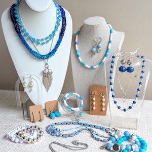 May include: A collection of blue and white jewellery including multiple layered necklaces, beaded bracelets, and various pairs of earrings. The set features silver-toned metal accents, pearl-like beads, turquoise-coloured glass beads, and a large silver leaf pendant.