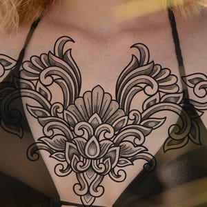 Puede incluir: Tatuaje temporal floral negro y gris en el pecho. El tatuaje presenta un patrón simétrico de hojas arremolinadas y una flor central. El diseño es detallado e intrincado, con sombreado para crear profundidad.