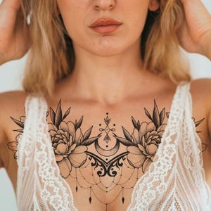 Puede incluir: Un diseño de tatuaje floral en blanco y negro en el pecho con dos grandes flores de peonía con hojas detalladas y una luna creciente. El tatuaje está centrado en el pecho e incluye delicados detalles de cadenas colgantes.