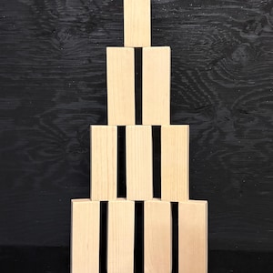 May include: A tower of light-colored wooden blocks, arranged in a pyramid shape. The blocks are rectangular and stacked on top of each other, creating a stable structure. The background is a dark, textured surface.