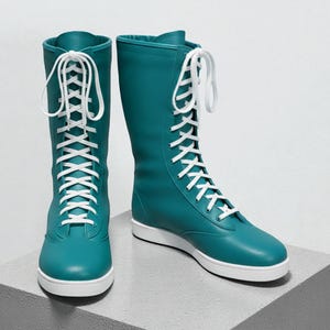 May include: A pair of teal-colored, knee-high boots with white laces and soles. The boots are made of a smooth material and are displayed on a gray, geometric surface. The laces run up the front of the boots, creating a striking contrast.