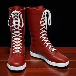 May include: A pair of tall, red boots with white laces and white soles. The boots are made of a smooth material and have a classic design. The laces are tightly laced up the front of the boots. The boots are set against a dark background.