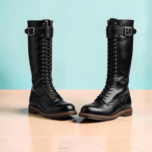 May include: A pair of black knee-high boots featuring a lace-up front with metal eyelets, a rounded toe, and a buckled strap at the top of the shaft. The boots have a dark brown sole with a visible welt and a low heel, constructed from smooth material.