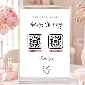 May include: A clear acrylic sign with the words "Scan to pay" in black script. Two QR codes are below the text, with "$Zelle" and "$ Cash App" written underneath. A heart and "Thank You" are at the bottom. Pink flowers and a vase are in the background.