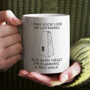 May include: White ceramic mug with a black and white illustration of a trig point and the text "I may look like I'm listening but in my head I'm planning a trig walk."